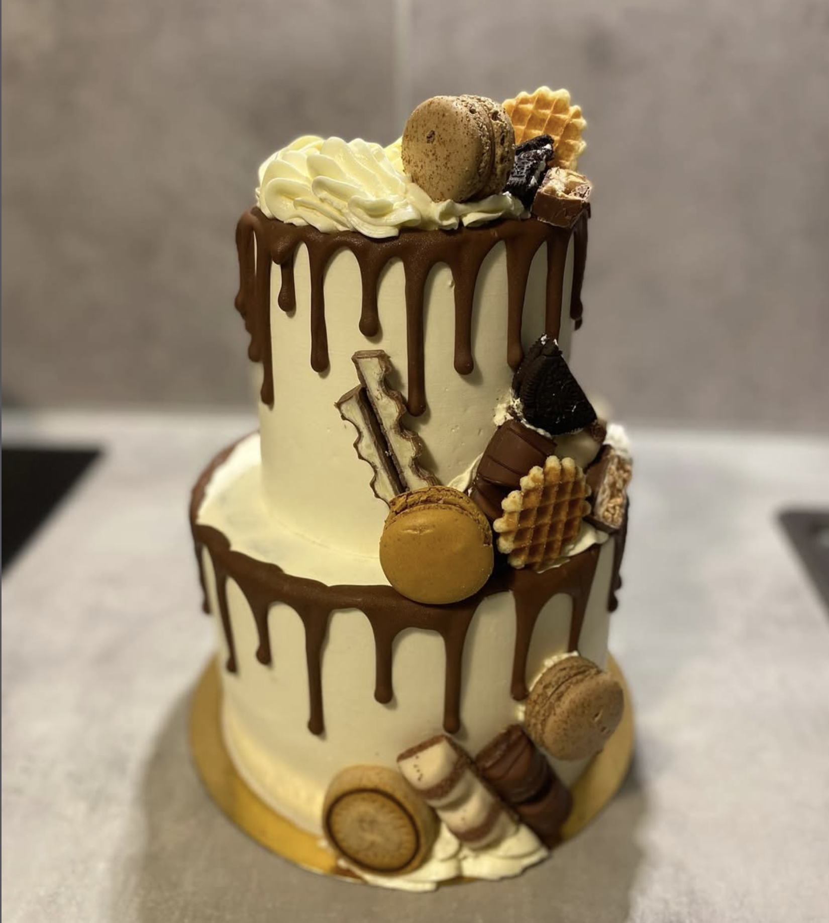 Drip Cake gourmand chocolat | Taasty Cakes Drip Cake gourmand chocolat — Un drip cake généreux décoré de macarons, biscuits, gaufrettes et gourmandises chocolatées sur une crème vanillée. | Taasty Cakes