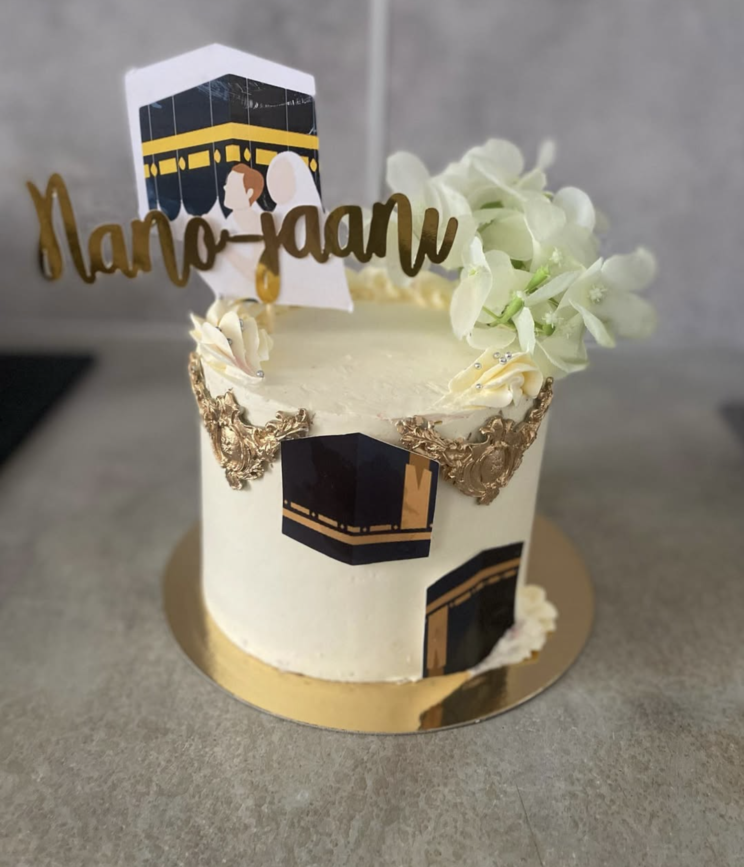 Gâteau mariage thème La Mecque | Taasty Cakes Gâteau mariage thème La Mecque — Un gâteau blanc et doré aux finitions élégantes, décoré sur le thème du mariage musulman avec topper personnalisé et mot | Taasty Cakes