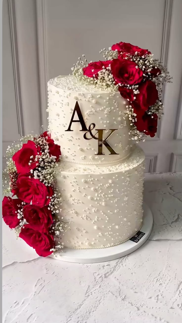 Gâteau de mariage personnalisé aux initiales | Taasty Cakes Gâteau de mariage personnalisé aux initiales — Une pièce montée blanche aux détails nacrés, décorée de roses rouges et personnalisée avec les initiales des mariés. | Taasty Cakes